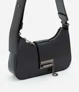 Cartera baguette pequeña de PU negro con acabado brillante, asa corta fija, cierre superior con cremallera y detalles metálicos. Incluye una cadena metálica decorativa en el frente.