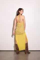 Vestido largo amarillo con escote halter y detalle de volados en el cuello. Presenta un diseño superpuesto con una capa superior estampada a cuadros multicolor con nudo lateral en la cintura y una falda fluida lisa con abertura lateral.