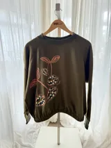 Buzo cropped de algodón color verde militar, con mangas ranglan y diseño estampado en el frente con motivos de besos y moños. Cuenta con elástico holgado en la cintura y los puños.
