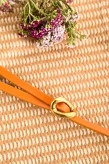 Cinto fino color naranja con hebilla dorada ovalada.