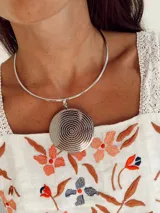 Gargantilla rígida en tono plateado con un dije circular grande de superficie texturizada con diseño de puntos concéntricos.