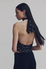 Top de satén con diseño tipo halter, escote alto con frunces frontales y bajo estilo globo. Presenta espalda abierta con cierre de botones forrados en la parte inferior.
