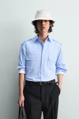 Camisa de algodón color celeste, corte relaxed fit, con cuello solapa, manga larga y trabillas en los hombros. Presenta dos bolsillos de plastrón con solapa en el pecho.