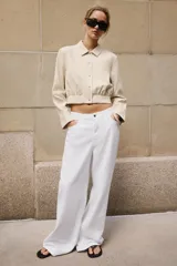 Camisa crop de manga larga con cuello solapa y cierre frontal de botones, confeccionada en tejido sintético con efecto piel color beige.