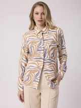 Camisa de manga larga con estampado de cebra en tonos beige, marrón y lila. Tiene cuello clásico, cierre con botones y un bolsillo en el pecho.