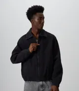 Campera estilo bomber de jean color negro, con cierre frontal, cuello clásico, mangas largas con puños elásticos y ruedo ajustable con elástico.