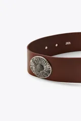 Cinturón ancho de cuero marrón con hebilla cuadrada metálica y apliques de flores metálicas plateadas.