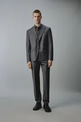 Pantalón de traje regular fit color gris oscuro, confeccionado en tejido con lana, con bolsillos frontales y bolsillos traseros de doble vivo con botón. Cierre frontal con cremallera y botón.