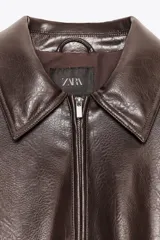 Chaqueta bomber de efecto piel en color marrón oscuro, con cuello solapa, cierre frontal de cremallera metálica, bolsillos laterales de vivo y mangas largas con puños elásticos. El bajo cuenta con ajuste elástico.