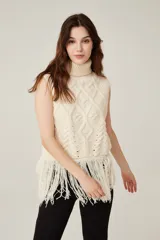 Chaleco de punto sin mangas con cuello polera, diseño de trenzas y rombos en relieve, y detalle de flecos largos en el ruedo.