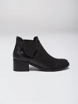 Bota tipo chelsea de cuero negro con paneles laterales elásticos y textura combinada. Presenta un taco cuadrado de altura media y punta redondeada.