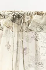 Shorts de tiro bajo confeccionado en viscosa, con estampado floral y paisley en tonos neutros. Presenta cintura elástica con detalle de volantes y lazada frontal.