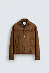 Cazadora de piel con acabado ante color marrón, corte relaxed fit, cuello bowling y manga larga con puño abotonado. Presenta bolsillos de vivo en la cadera y cierre frontal de botonadura.