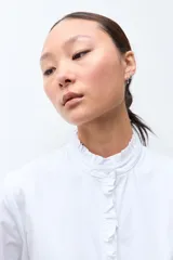 Camisa blanca de manga larga con cuello alto y volados en el cuello y puños.