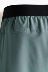 Short deportivo de doble capa color verde con calzas cortas negras incorporadas en el interior. Cuenta con tecnología DryMove™, cintura elástica negra con cordón ajustable, bolsillos laterales y aberturas en el bajo.