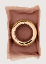 Pulsera rígida de metal dorado con diseño ancho, voluminoso y acabado brillante.