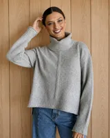 Polerón de lana lambswool color gris, con cuello alto, diseño holgado y costura central vertical. Presenta puños y ruedo acanalados con un corte ligeramente más corto en el frente.
