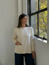 Sweater de punto color beige, con cuello redondo, manga larga y dos bolsillos frontales tipo parche.