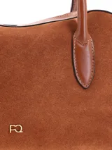 Cartera tipo bowling de cuero gamuza color tostado, con doble asa de mano en cuero liso, cierre superior y logo metálico de la marca en el frente.