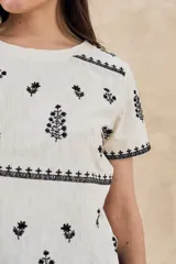Remera de algodón color blanco con bordados florales y geométricos en color negro. Presenta cuello redondo, mangas cortas y un diseño con franjas horizontales bordadas.