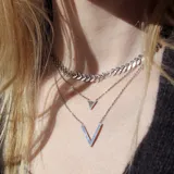 Collar doble plateado con cadena fina. El collar más corto tiene un dije triangular con un pequeño cristal en el centro. El collar más largo tiene un dije en forma de V.