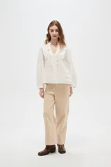 Blusa de viscosa color blanco, con cuello en V, detalles de volados y frunces en el frente, y mangas largas abullonadas con puños ajustados.