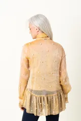 Blusa dorada de organza plisada con bordado de perlas, lazo en el cuello y musculosa debajo.