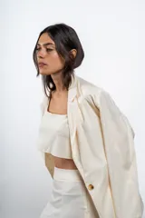 Blazer de lino color crema, con solapas clásicas y cierre frontal de un botón. Presenta un corte estructurado y elegante.