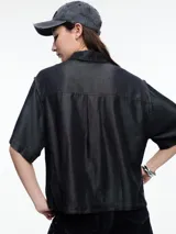 Camisa negra de manga corta confeccionada en denim liviano de tencel, de calce cuadrado y relajado. Presenta cierre frontal con tapeta escondida y costuras en color contraste.