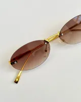 Lentes de sol ovalados con marco dorado y lentes degradé color marrón.