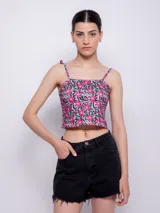 Top corto con escote recto y tirantes finos ajustables mediante nudo en los hombros. Presenta un estampado floral sobre fondo oscuro, con flores rosadas y hojas turquesas.