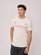 Remera color crema de hombre, marca Rusty, con estampado frontal en color rojo con el logo de la marca y la leyenda "Rusty Worldwide Supply Co. Since 1985".