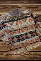 Campera beige con estampado azteca en tonos marrón, naranja y azul marino. Tiene cuello de corderito color beige, cierre con botones a presión, dos bolsillos laterales y puños con botón.
