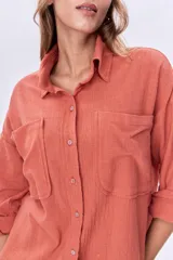 Camisa color coral de corte holgado, con cuello clásico, cierre frontal con botones, mangas largas con puños abotonados, dos bolsillos de parche en el pecho y ruedo asimétrico.