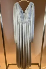 Vestido largo de fiesta en color negro con acabado brillante. Presenta un escote en V, cintura entallada con detalle de cinturón fino y mangas largas tipo capa con efecto plisado.