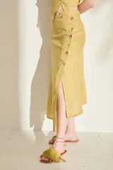 Falda midi verde de lino, con diseño asimétrico, tajito frontal y cierre lateral con botones de madera con ojales bordados.