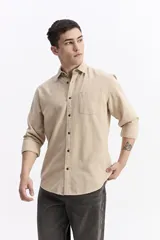 Camisa de manga larga con textura, color beige, con cuello clásico, cierre frontal de botones y un bolsillo en el pecho.