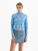 Top de cuello polera y mangas largas, confeccionado en tela de punto con estampado de corazones atravesados por flechas sobre fondo azul. Presenta un diseño ajustado al cuerpo.