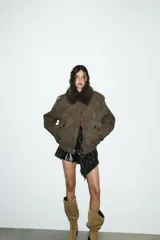 Cazadora color verde militar con efecto ante, cuello solapa con aplicación de pelo sintético desmontable, manga larga con puño, trabillas en los hombros y bolsillos frontales con solapa y botón. Cierre frontal con cremallera y botones ocultos.