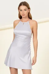 Vestido corto de satén color lila, con escote halter y espalda descubierta con tiras para atar. Presenta una hilera de botones decorativos en el lateral y falda con caída fluida.