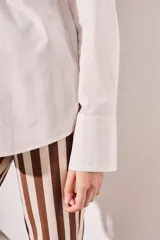 Camisa blanca oversize de algodón, con cuello clásico, cierre frontal con botones de nácar y bolsillo en el pecho.