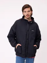 Campera reversible con capucha oculta, confeccionada en sarga de algodón con elastano en el exterior y nylon de poliéster en el interior. Presenta cierre frontal con botones a presión, costuras visibles en contraste y puños elásticos.