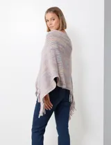 Poncho tejido en hilo soft, con efecto jaspeado multicolor (predominantemente tonos oscuros como azul marino, negro, y toques de violeta y dorado/lurex). Presenta un diseño asimétrico y flecos largos en los bordes.
