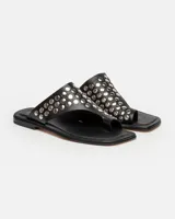 Sandalias planas blancas de cuero, con tira ancha sobre el empeine adornada con tachas plateadas.
