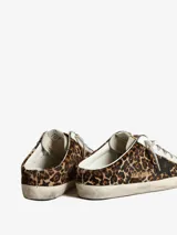 Zuecos Golden Goose modelo Super-Star Sabot, con diseño de zapatilla sin talón. Presentan exterior cubierto de glitter negro y dorado, estrella característica en el lateral, cordones y forro interior de shearling sintético.