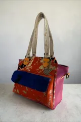 Cartera de cuero de diseño exclusivo con intervención artística de Carolina De Cunto, combinando tonos naranja, azul y detalles en color natu y terra. Cuenta con doble asa de hombro, solapa frontal de pelo sintético azul y herrajes metálicos.