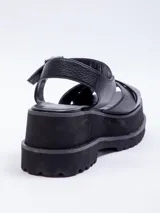 Sandalias negras de plataforma con doble cinta cruzada sobre el empeine y agarre mediante hebilla en el tobillo.