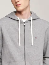 Buzo de felpa gris jaspeado con capucha y cordones blancos, cierre frontal de cremallera y bolsillos canguro. Presenta un pequeño logo bordado en el pecho.