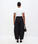Pantalón barrel de viscosa color negro, de corte ancho con diseño redondeado en las piernas y bajo ajustado. Presenta pinzas laterales, trabillas y un cinturón fijo de PU con hebilla metálica.