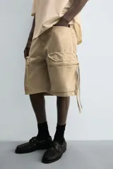 Bermuda de corte relajado en denim de algodón color beige, estilo cargo, con cinco bolsillos y bolsillos plastrón con solapa en las perneras.